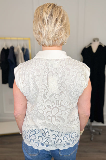 Back view of woman wearing Swagger Boutique’s Ivory Lace Sleeveless Top with jeans with clothing hanging in the background.