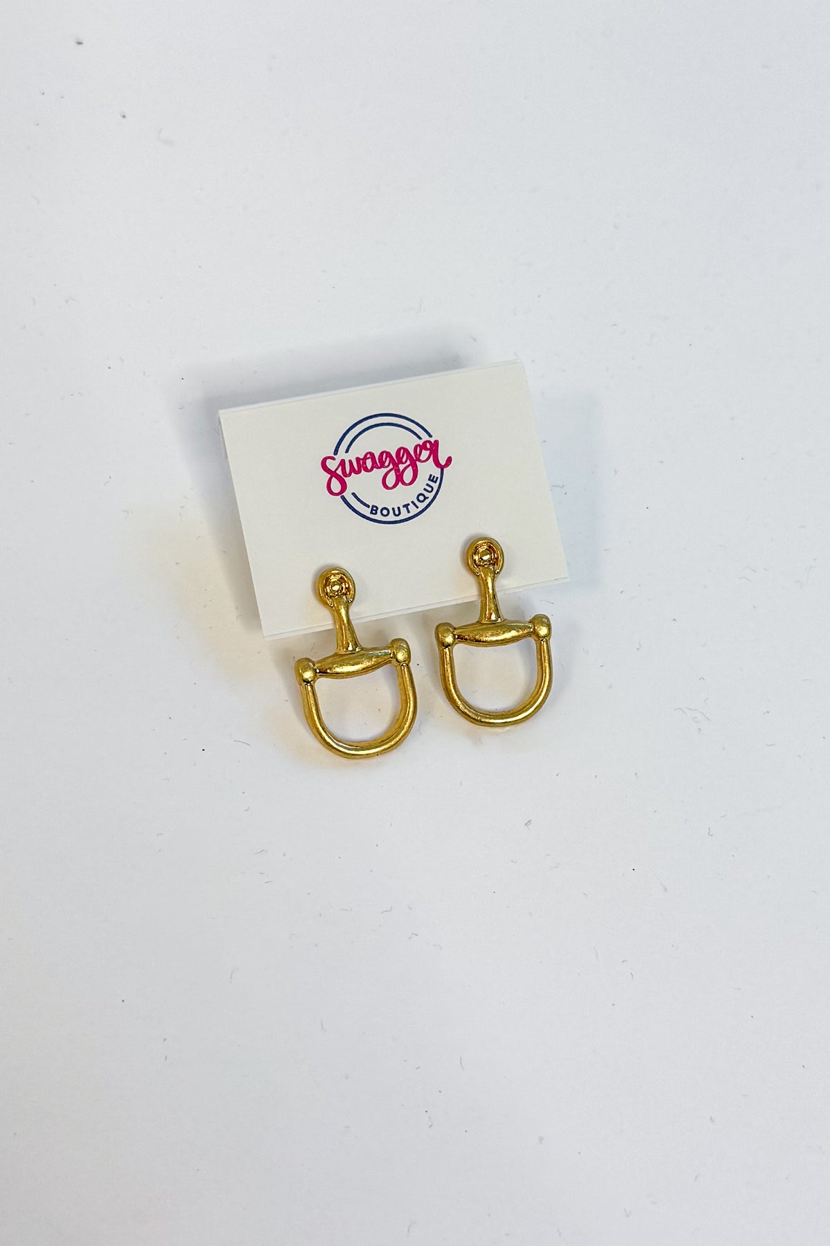 A pair of gold horsebit stud earrings displayed on a small white card with the &