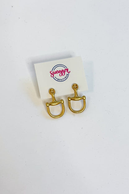 A pair of gold horsebit stud earrings displayed on a small white card with the &