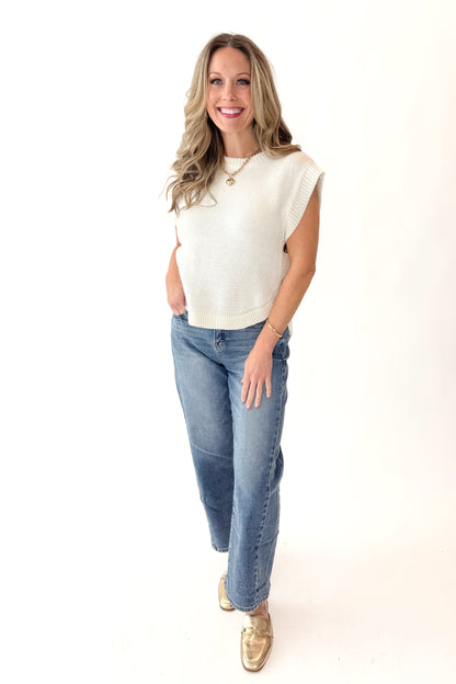 Front view of woman wearing Cream Side Button Detail Sleeveless Sweater with jeans against white studio background.