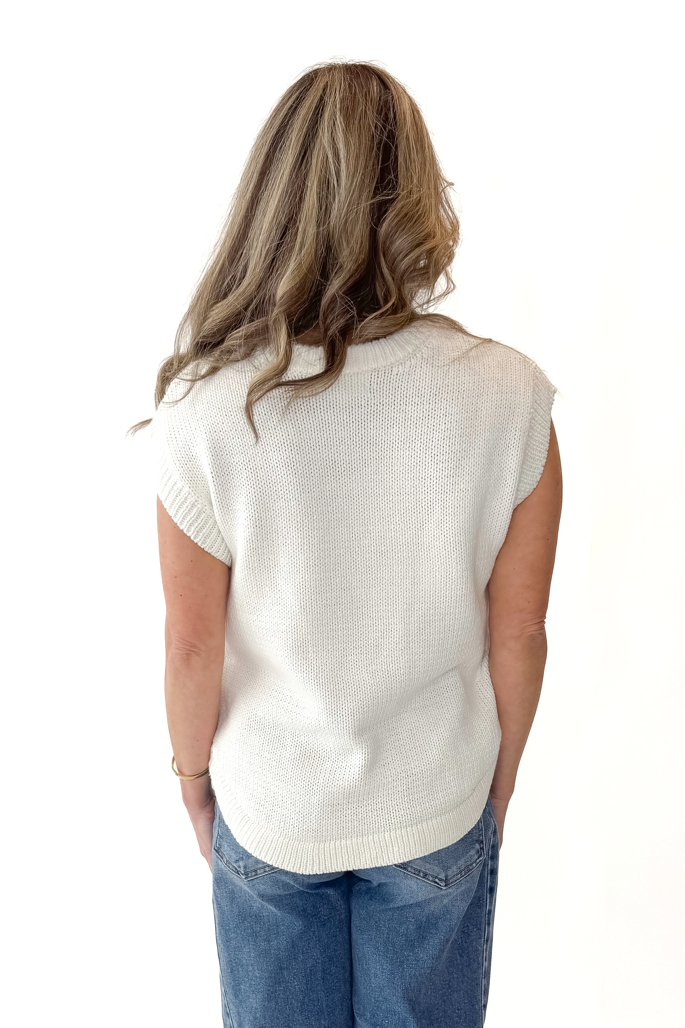 Back view of woman wearing Cream Side Button Detail Sleeveless Sweater with jeans against white studio background.