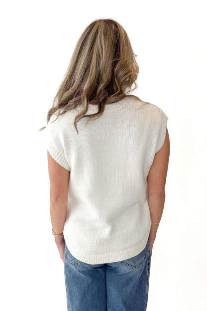 Back view of woman wearing Cream Side Button Detail Sleeveless Sweater with jeans against white studio background.