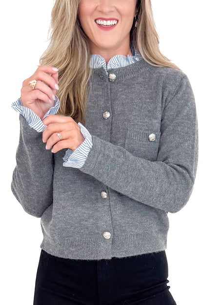 Woman wearing a gray cardigan with a striped shirt underneath on a white background