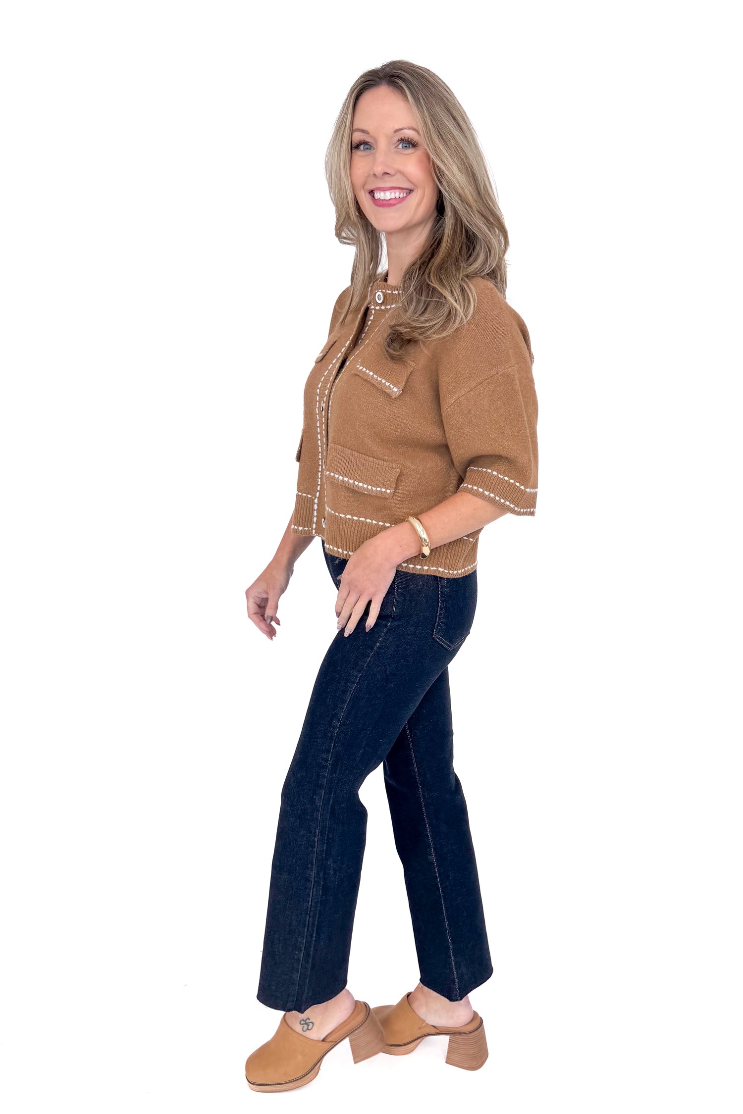 Side view of woman wearing camel stitch detail sweater with jeans against white studio background.