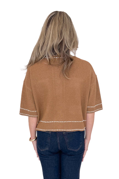 Back view of woman wearing camel stitch detail sweater with jeans against white studio background.