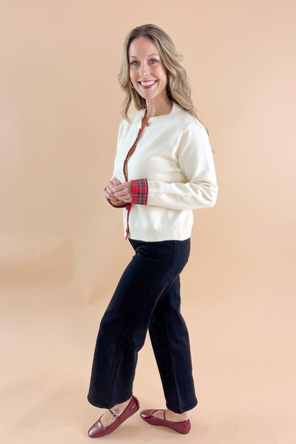 Side view of woman wearing Cream With Tartan Detail Button Up Cardigan with jeans against tan studio background.
