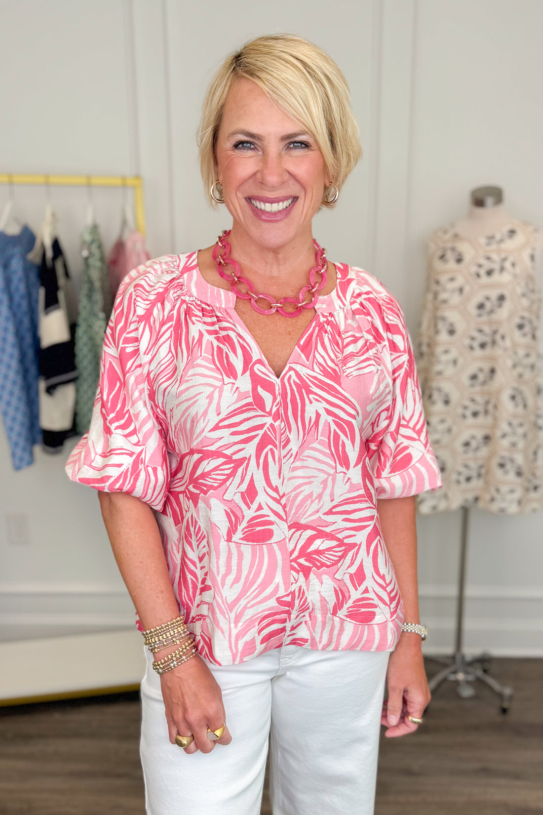 Woman wearing a pink leaf-patterned blouse in a clothing store.