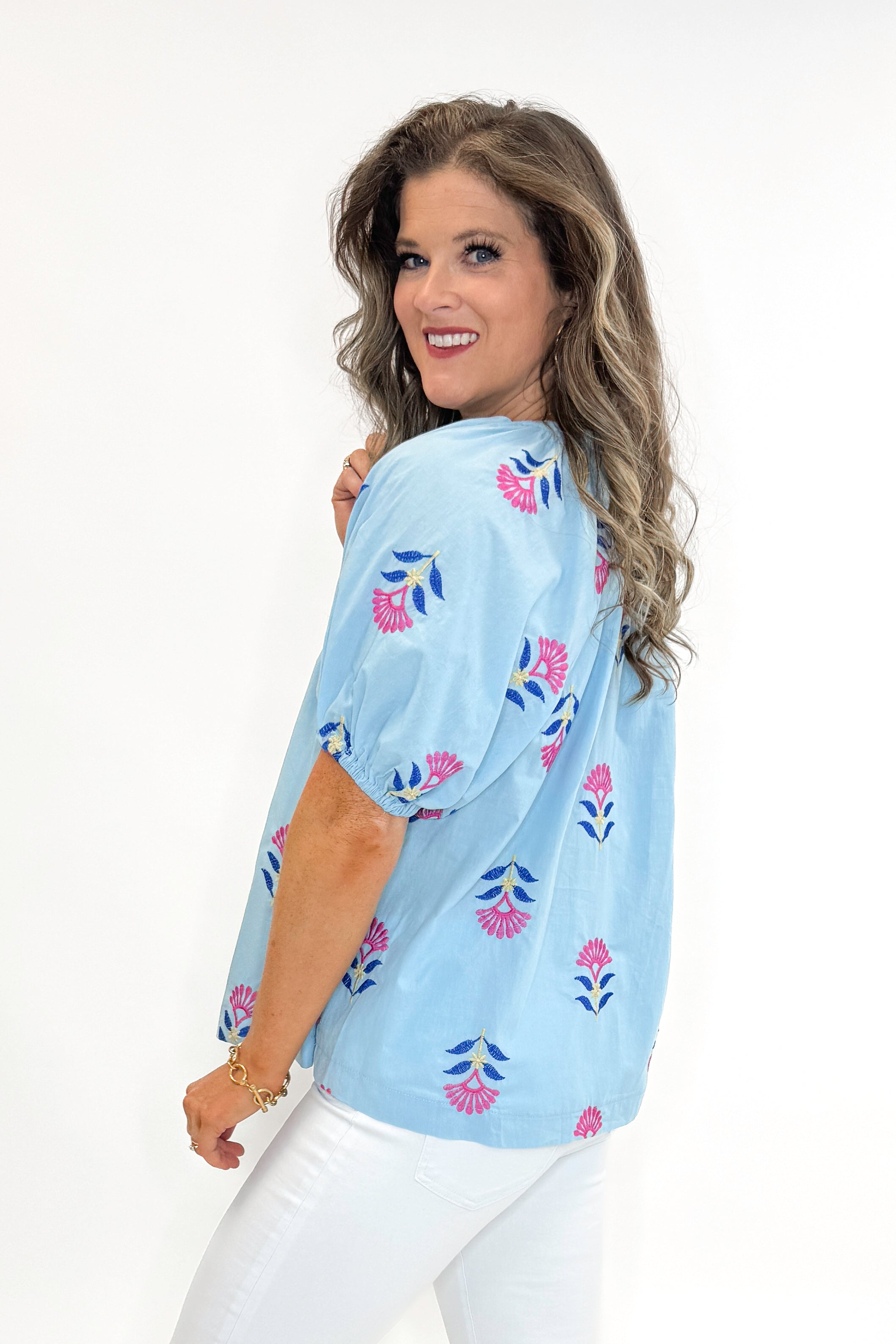 Side view of woman wearing Blue &amp; Multi Floral Embroidered Top with jeans against white studio background.