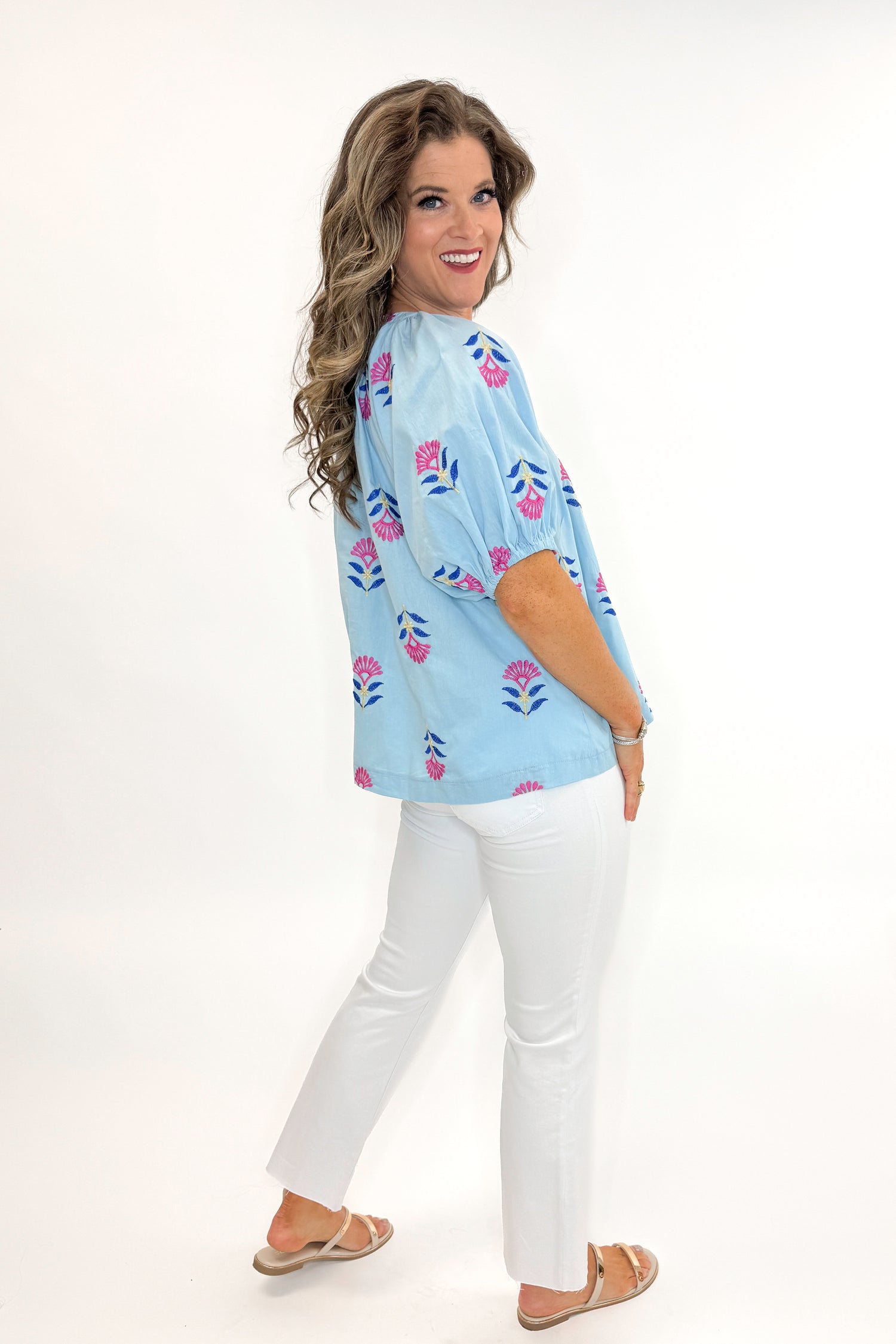 Side view of woman wearing Blue &amp; Multi Floral Embroidered Top with jeans against white studio background.