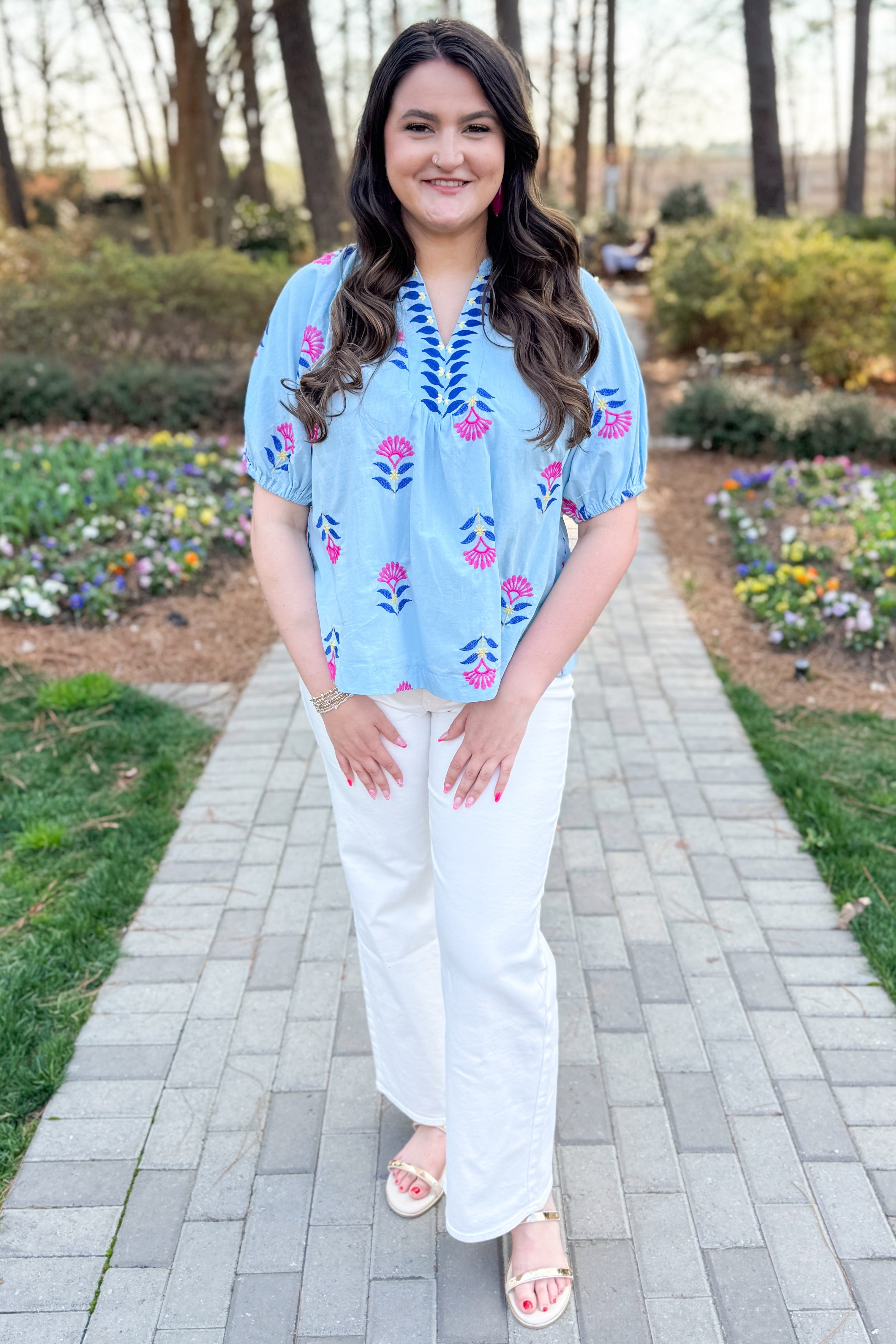 Front view of woman wearing Blue &amp; Multi Floral Embroidered Top with jeans at an outdoor garden area.