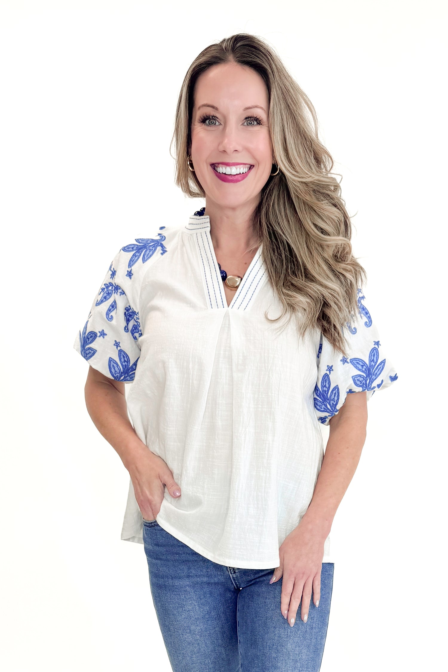 Front view of woman wearing Off White With Blue Embroidered Sleeve Top with jeans against white studio background.