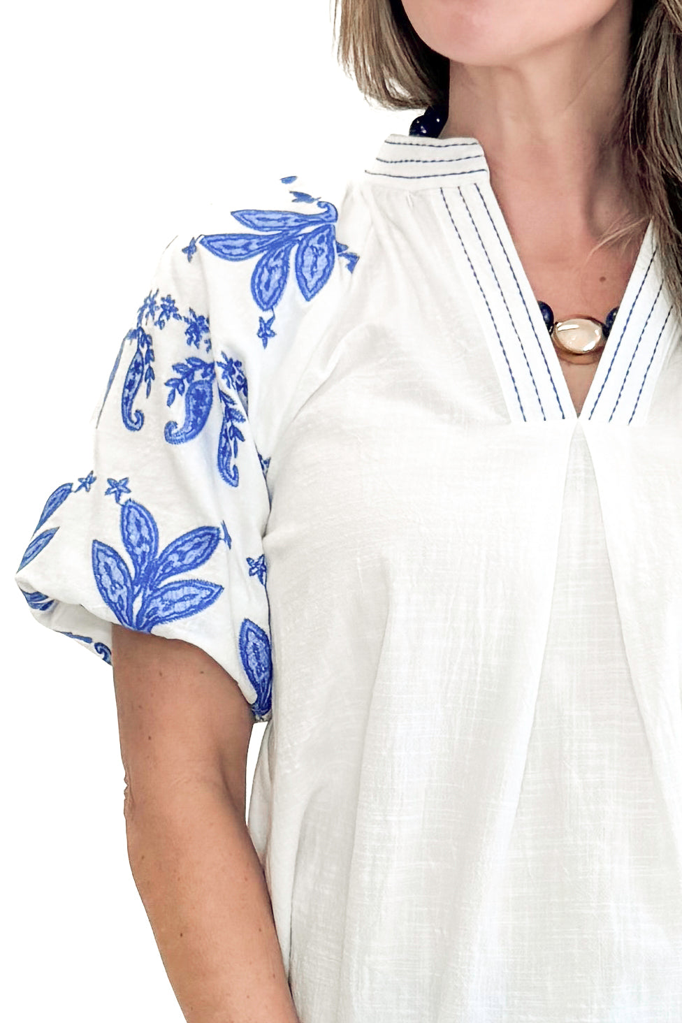 Front detail view of woman wearing Off White With Blue Embroidered Sleeve Top with jeans against white studio background.
