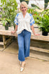Front view of woman wearing Off White With Blue Embroidered Sleeve Top with jeans at a garden center.