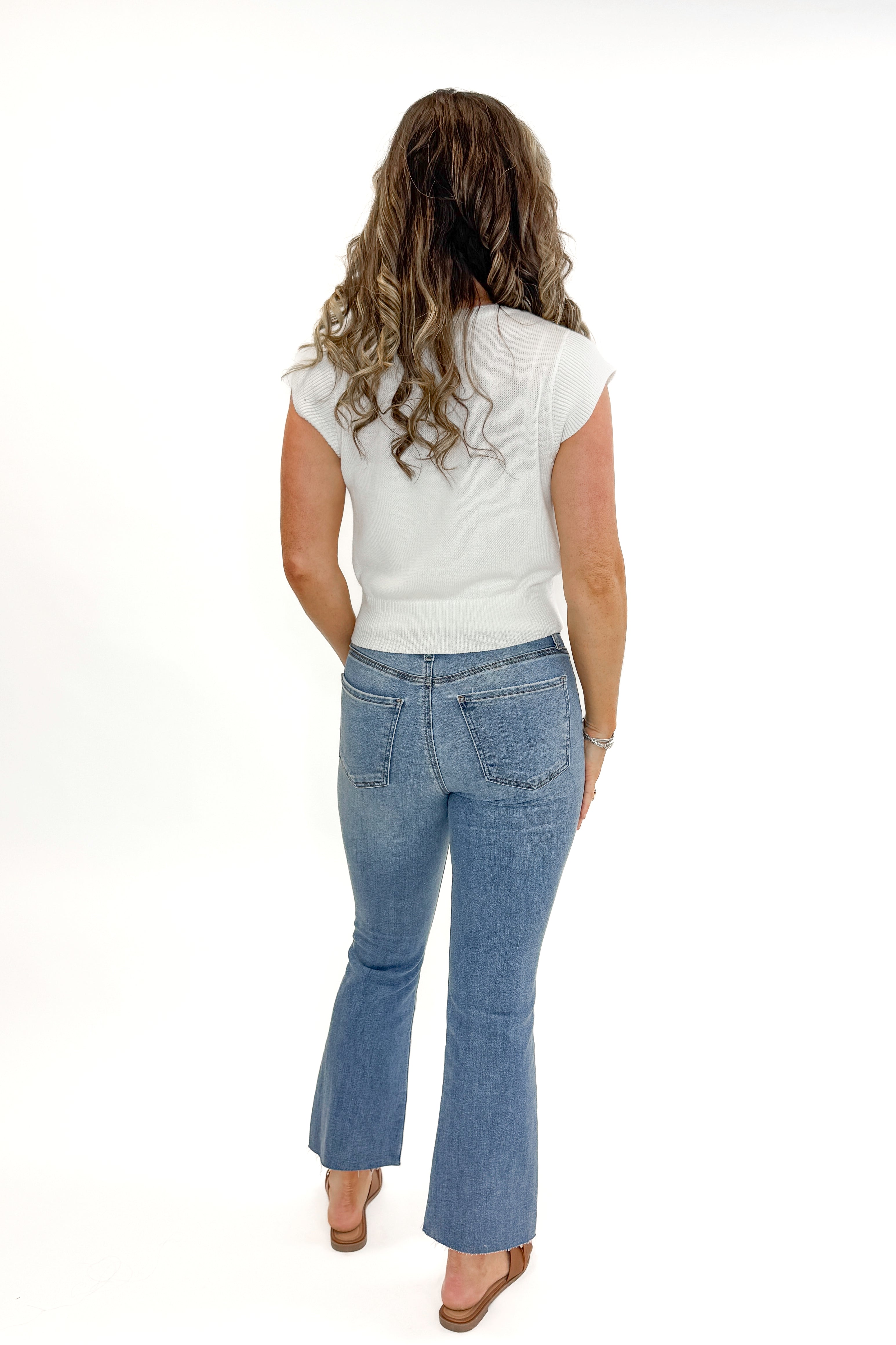 Back view of woman wearing Kelsey Ankle Flare Jeans In Medium Wash- Achievement by Kut from the Kloth with white sweater against white studio background.