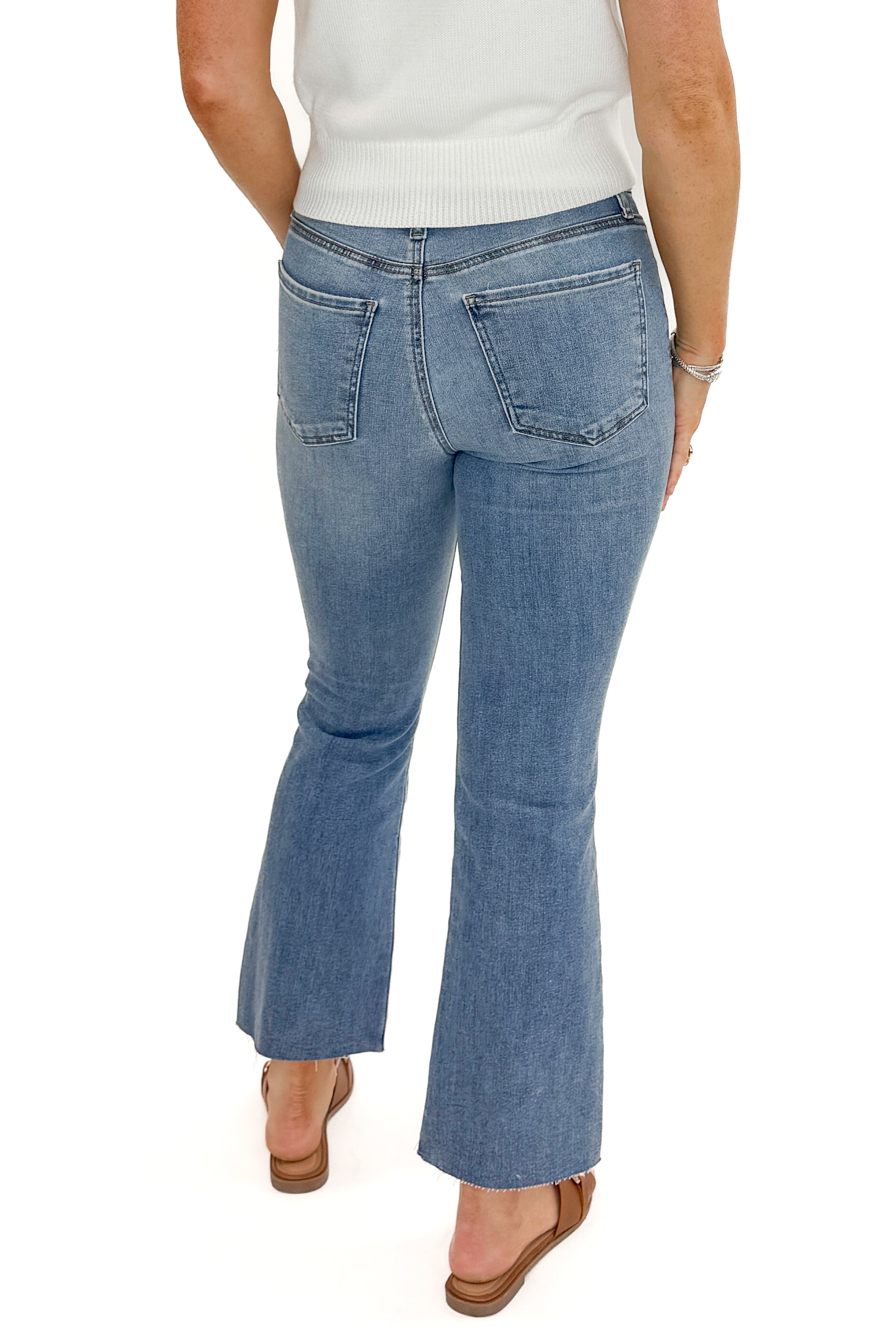 Back view of woman wearing Kelsey Ankle Flare Jeans In Medium Wash- Achievement by Kut from the Kloth with white sweater against white studio background.
