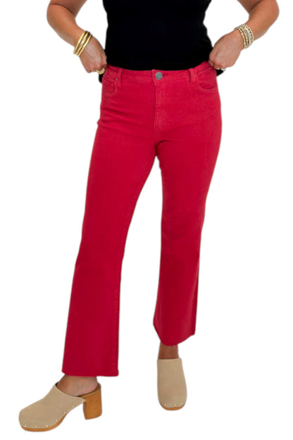 Front view of woman wearing Swagger Boutique’s Kelsey Ankle Flare Jeans In Ruby Red by Kut from the Kloth with black top against white studio background.