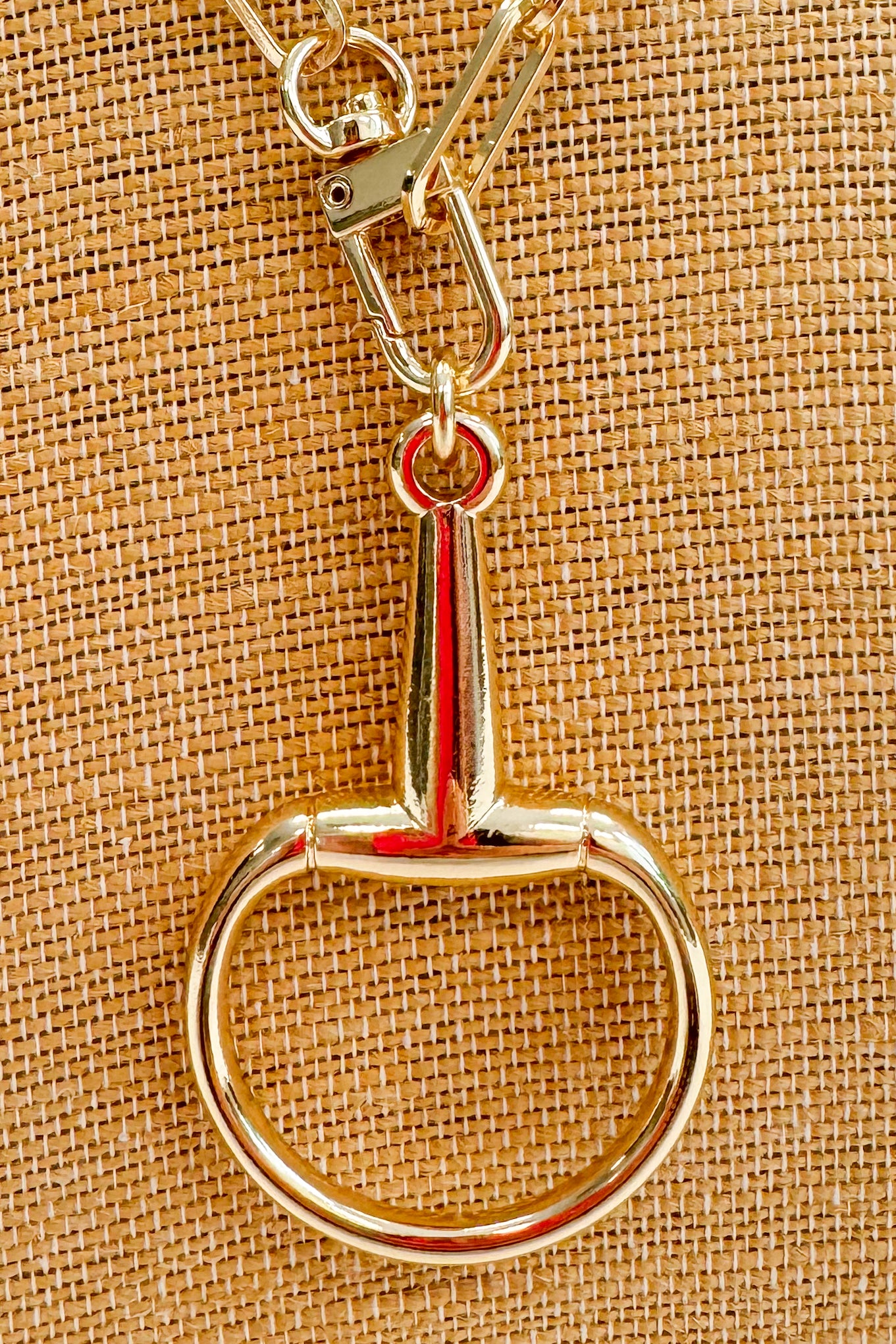 Gold horse bit pendant on a textured beige background