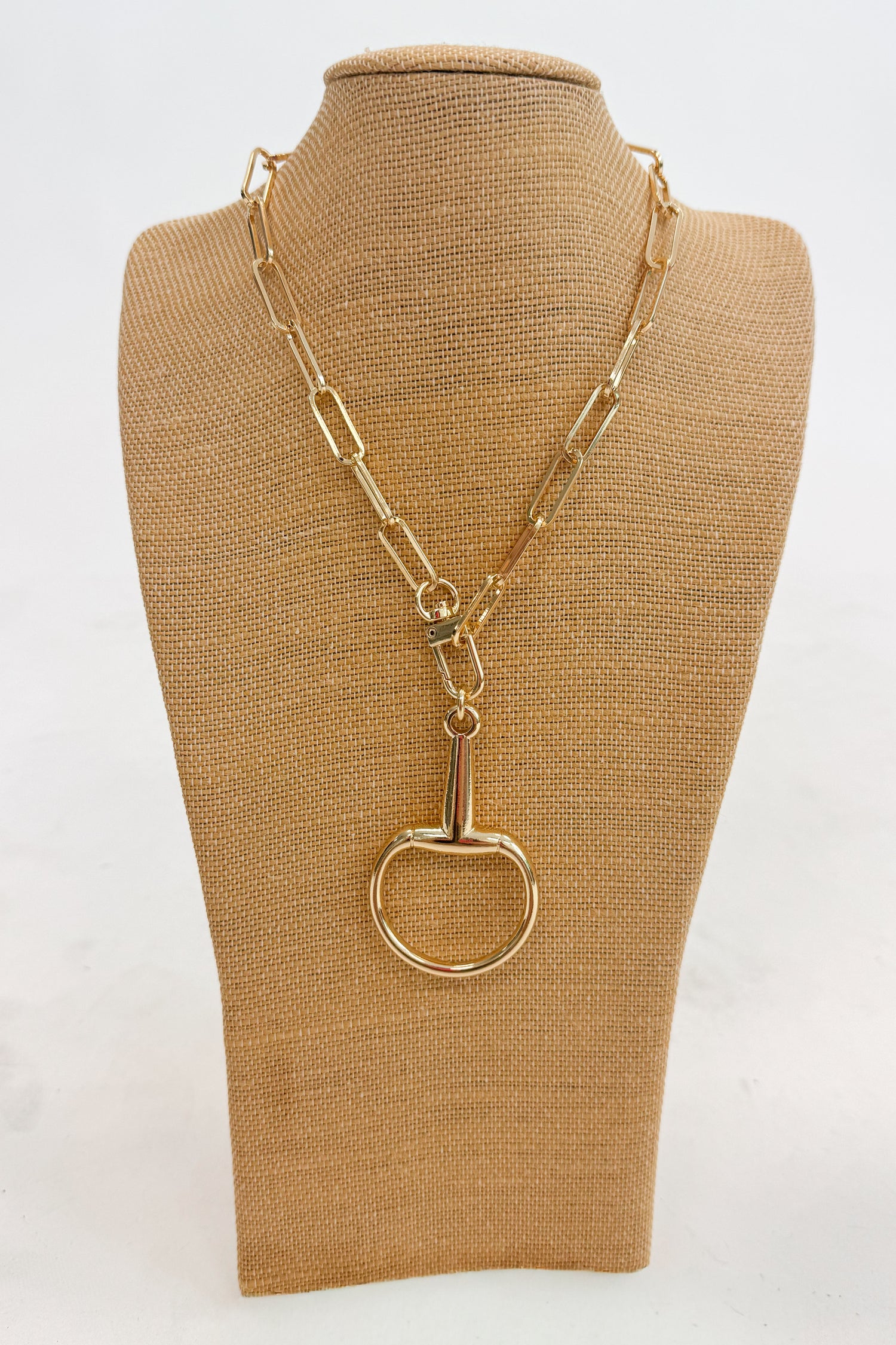 Gold necklace with a large horsebit pendant on a brown mannequin bust against a white background