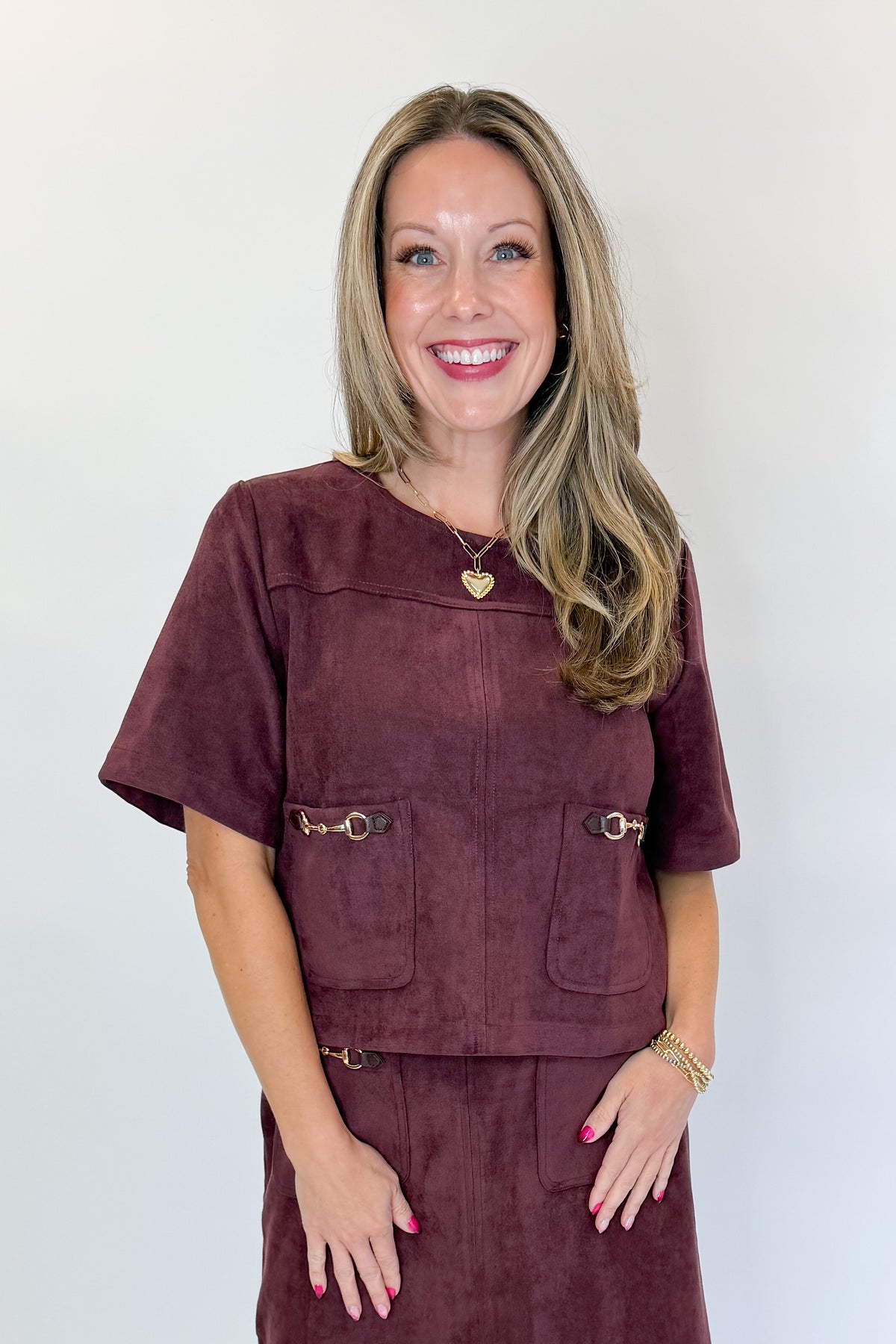Front view of woman wearing Swagger Boutique’s Merlot Suede Horsebit Pocket Top &amp; Skirt by Entro against white studio background.