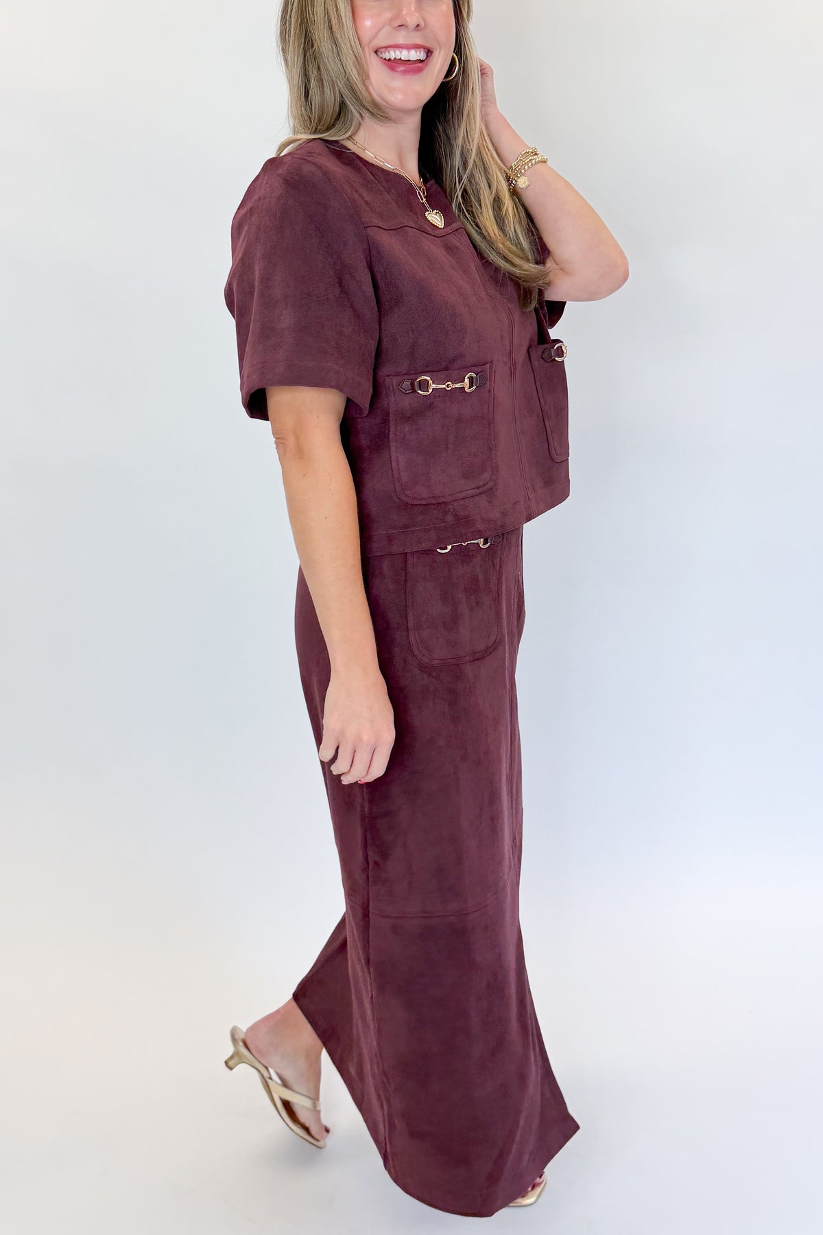Side detail view of woman wearing Swagger Boutique’s Merlot Suede Horsebit Pocket Top &amp; Skirt by Entro against white studio background.