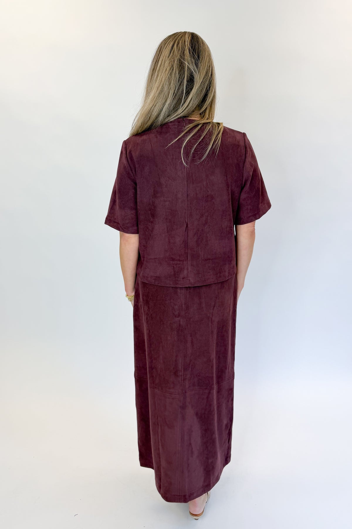 Back view of woman wearing Swagger Boutique’s Merlot Suede Horsebit Pocket Top &amp; Skirt by Entro against white studio background.