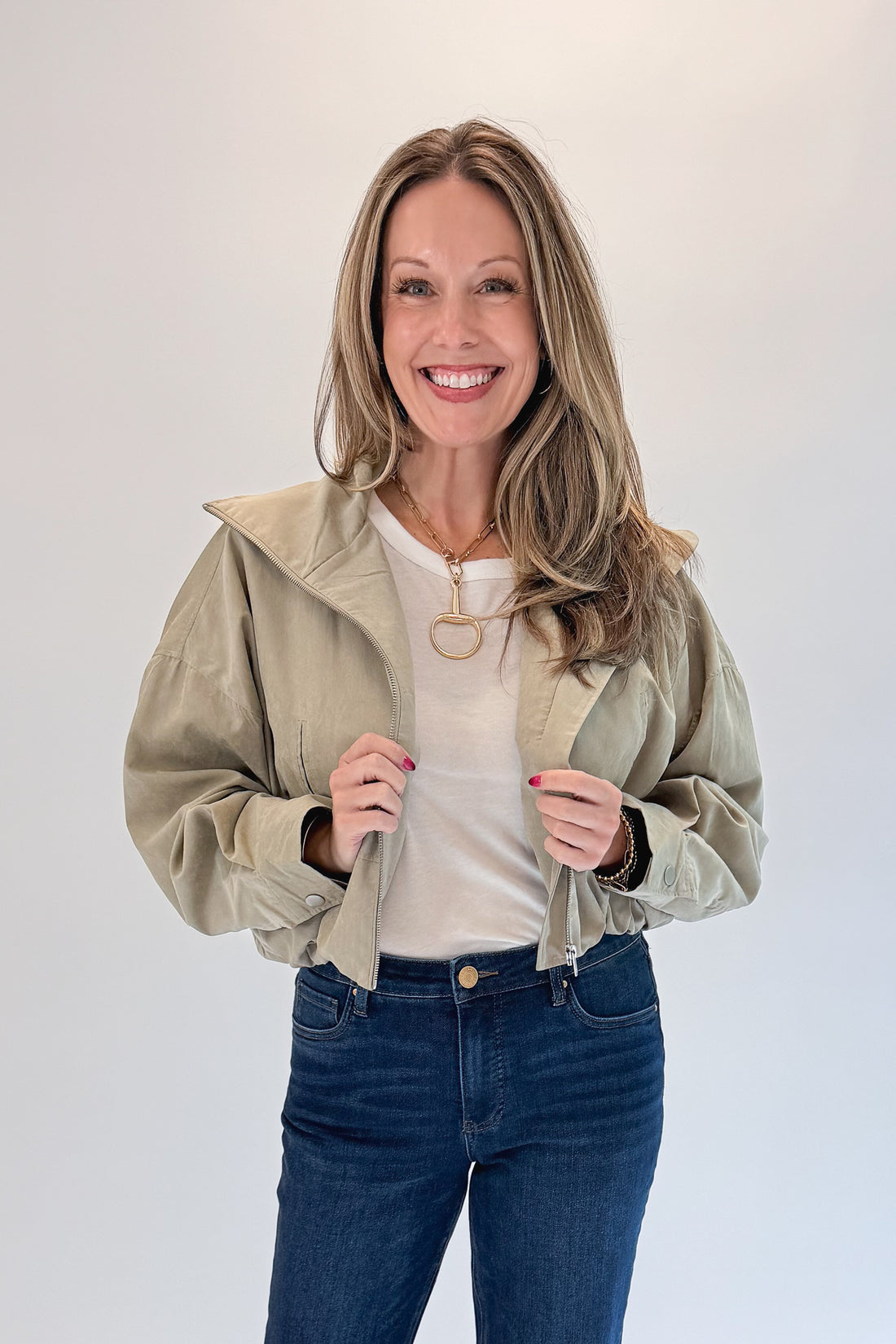 Front view of woman wearing Swagger Boutique’s Khaki Bubble Hem Bomber Jacket with jeans against white studio background.