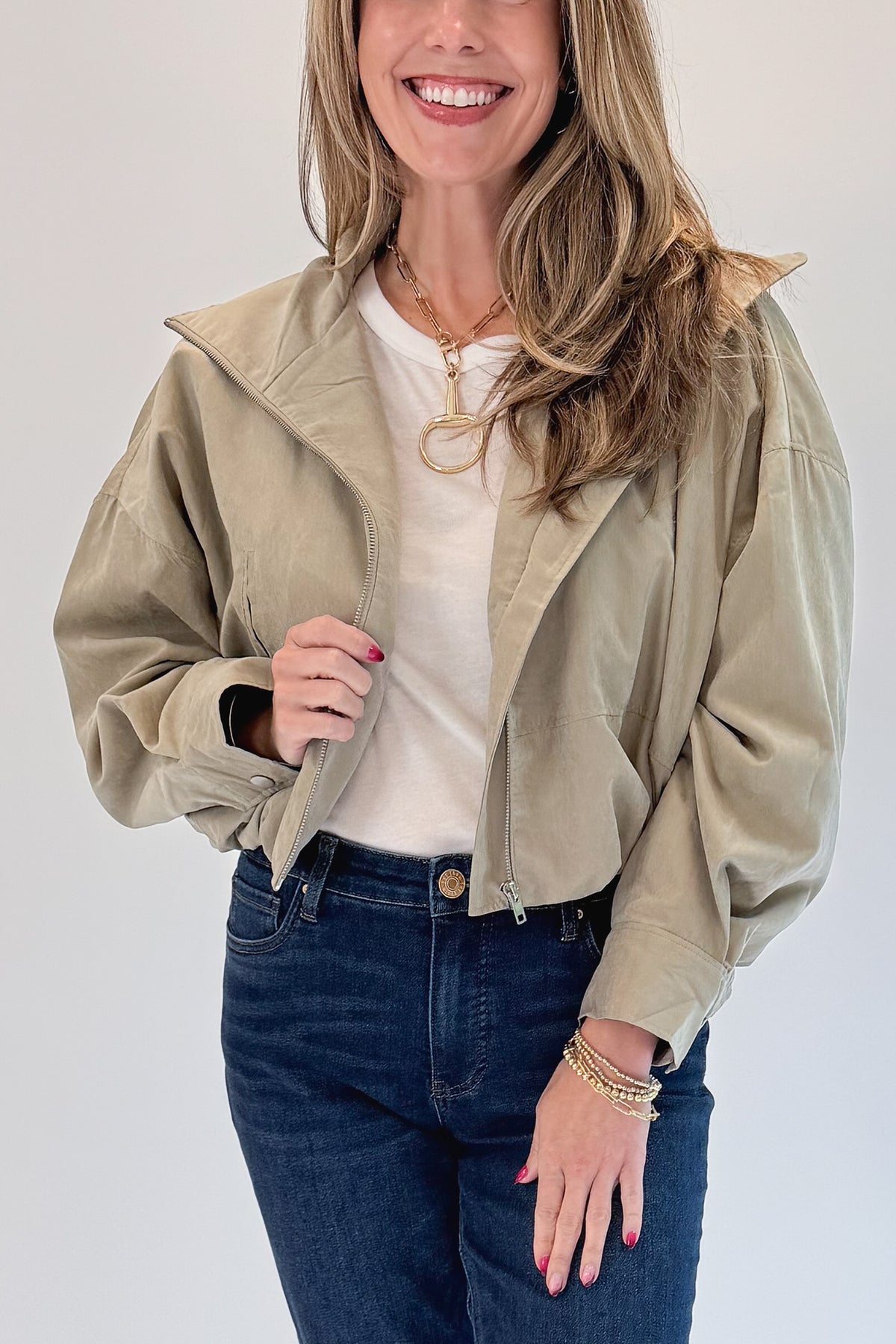 Front detail view of woman wearing Swagger Boutique’s Khaki Bubble Hem Bomber Jacket with jeans against white studio background.