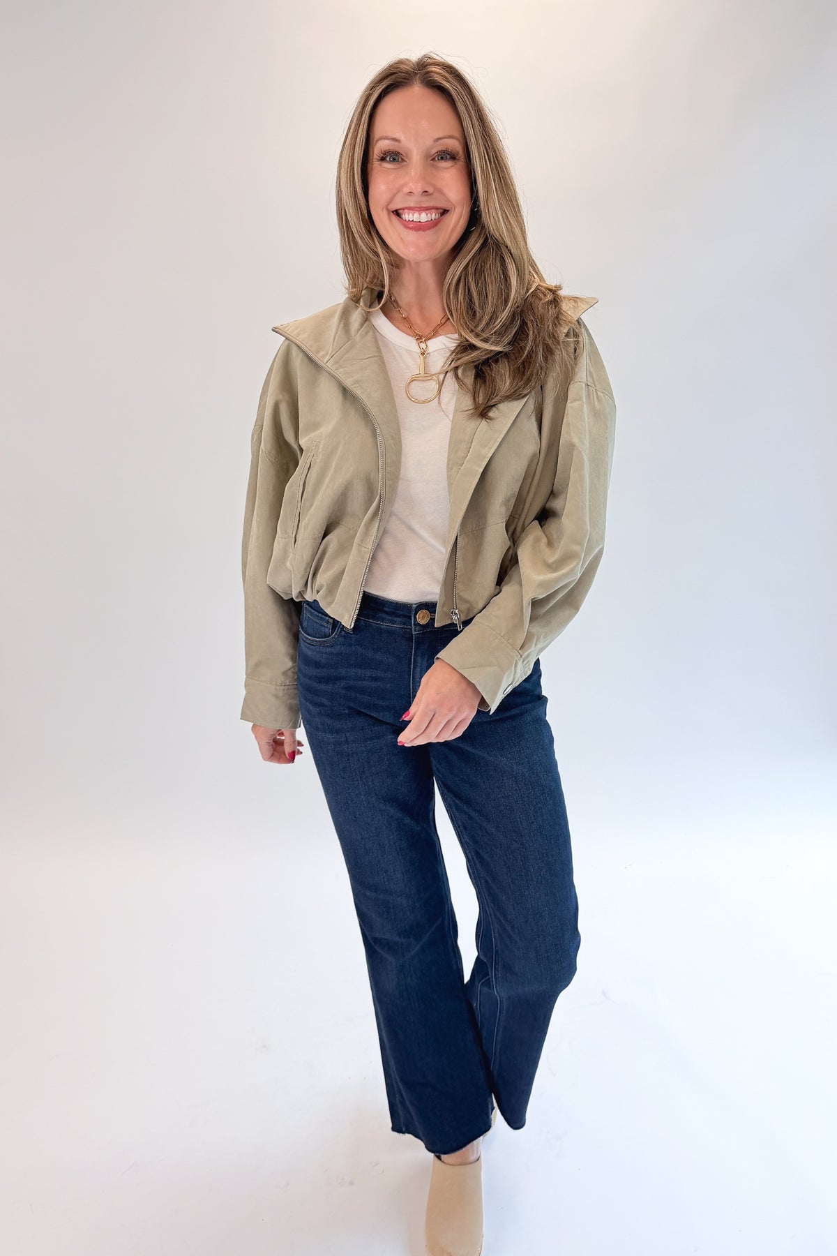 Front view of woman wearing Swagger Boutique’s Khaki Bubble Hem Bomber Jacket with jeans against white studio background.