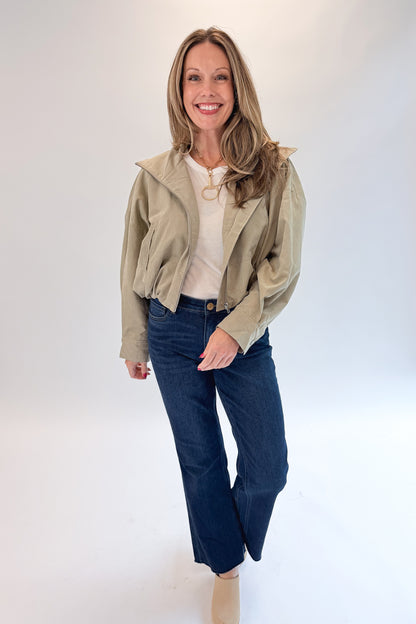 Front view of woman wearing Swagger Boutique’s Khaki Bubble Hem Bomber Jacket with jeans against white studio background.