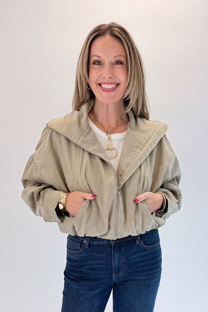 Front view of woman wearing Swagger Boutique’s Khaki Bubble Hem Bomber Jacket with jeans against white studio background.
