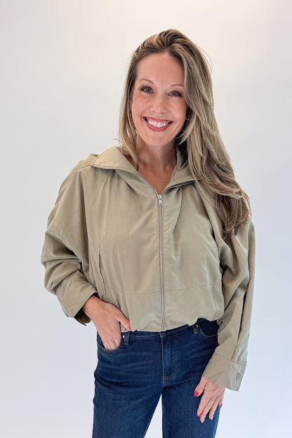 Front view of woman wearing Swagger Boutique’s Khaki Bubble Hem Bomber Jacket with jeans against white studio background.