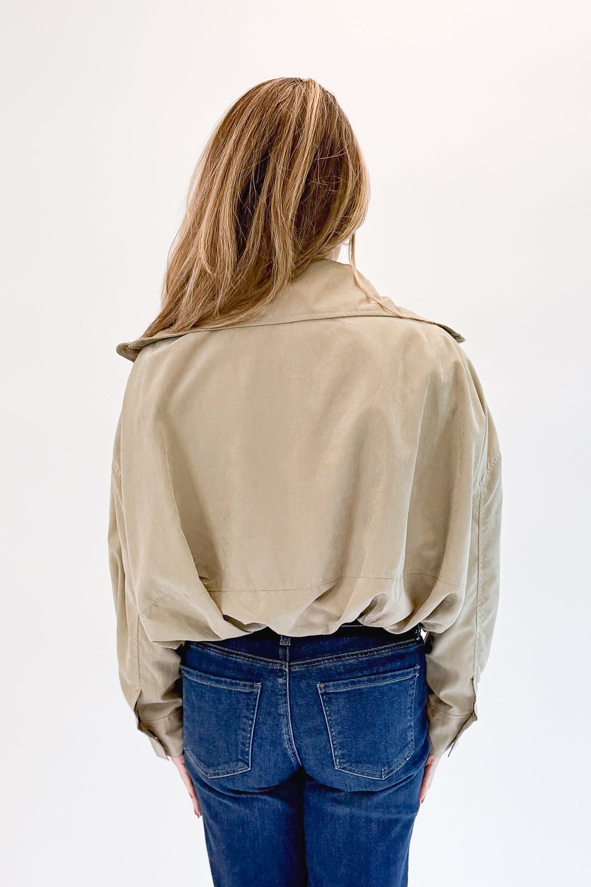 Back view of woman wearing Swagger Boutique’s Khaki Bubble Hem Bomber Jacket with jeans against white studio background.