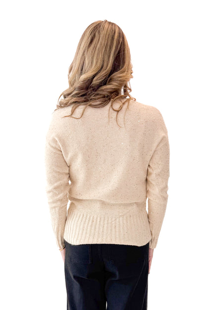 Back view of woman wearing Cream With Gold Sequin Sweater with jeans against white studio background.