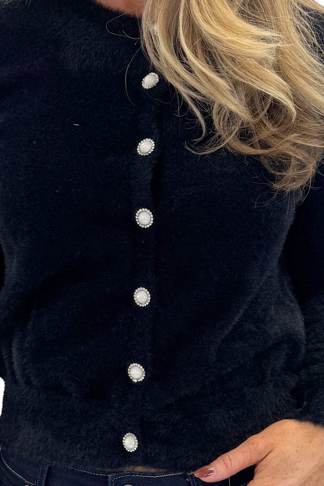 Front detail view of woman wearing Black With Rhinestone Buttons Eyelash Cardigan with jeans against white studio background. 