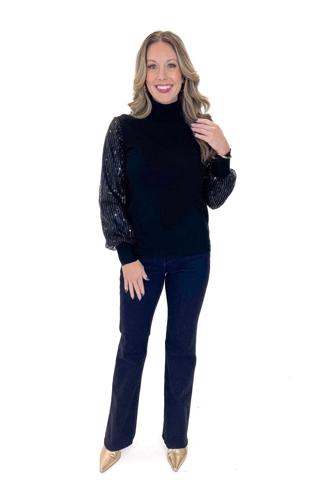 Front view of woman wearing Black Sequined Sleeve Turtleneck Sweater with jeans against white studio background.