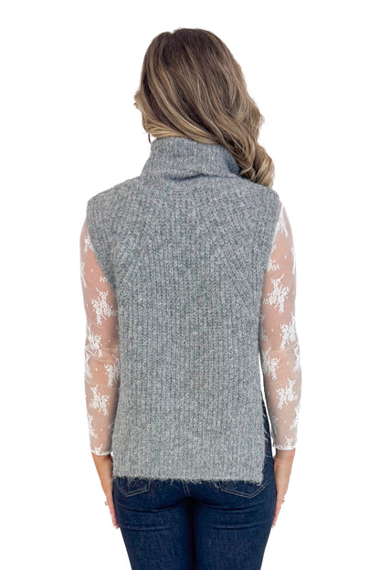 Back view of woman wearing Grey Turtleneck Sweater Vest and blue jeans.