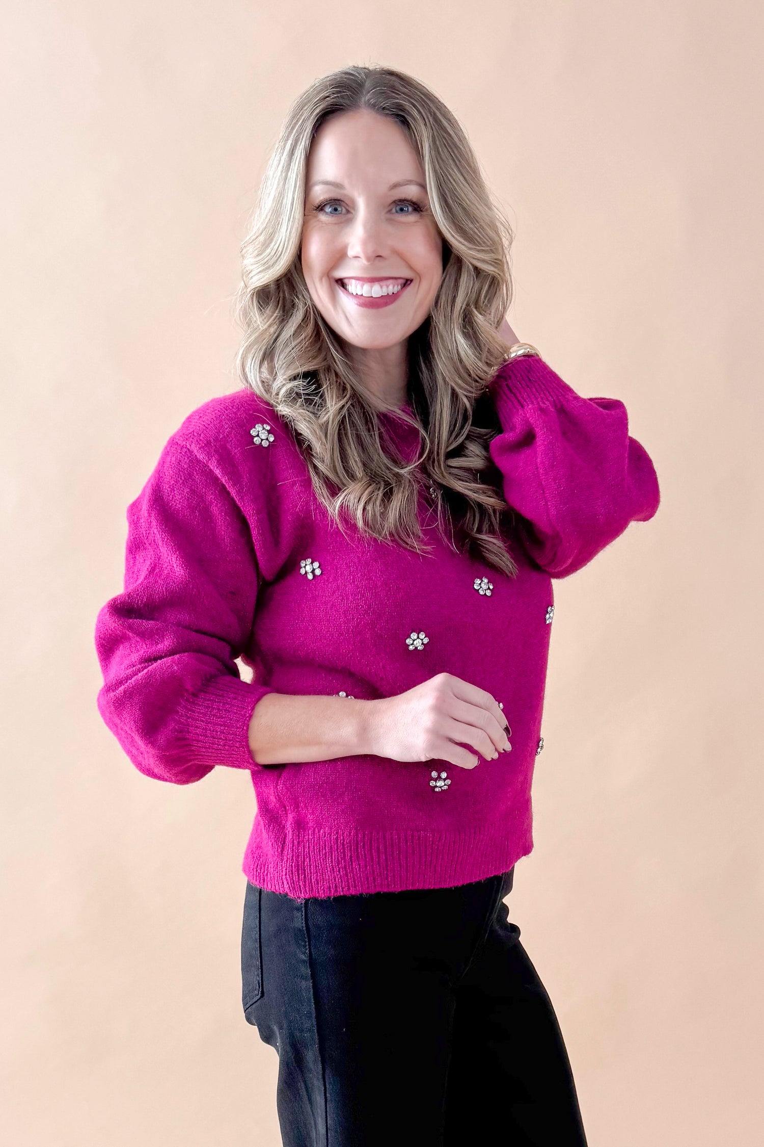 Side view of woman wearing Magenta Rhinestone Detail Sweater with jeans against tan studio background.