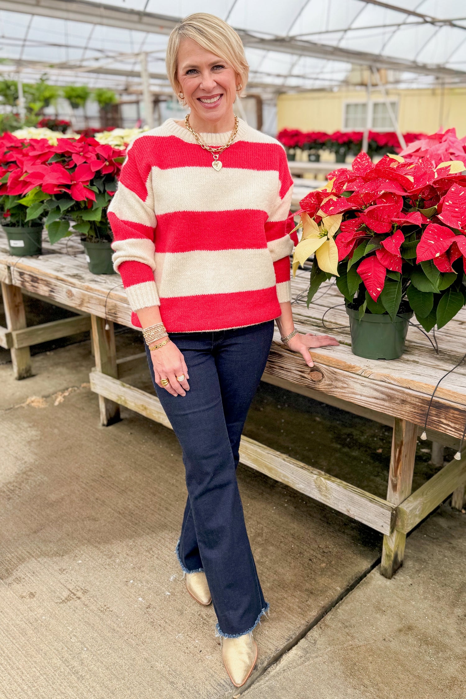 Front view of woman wearing Ivory &amp; Red Striped Sweater with jeans by holiday decor.