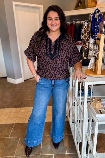 Front view of woman wearing Swagger Boutique’s Leopard Half Zip Top by Entro with jeans standing at the store.