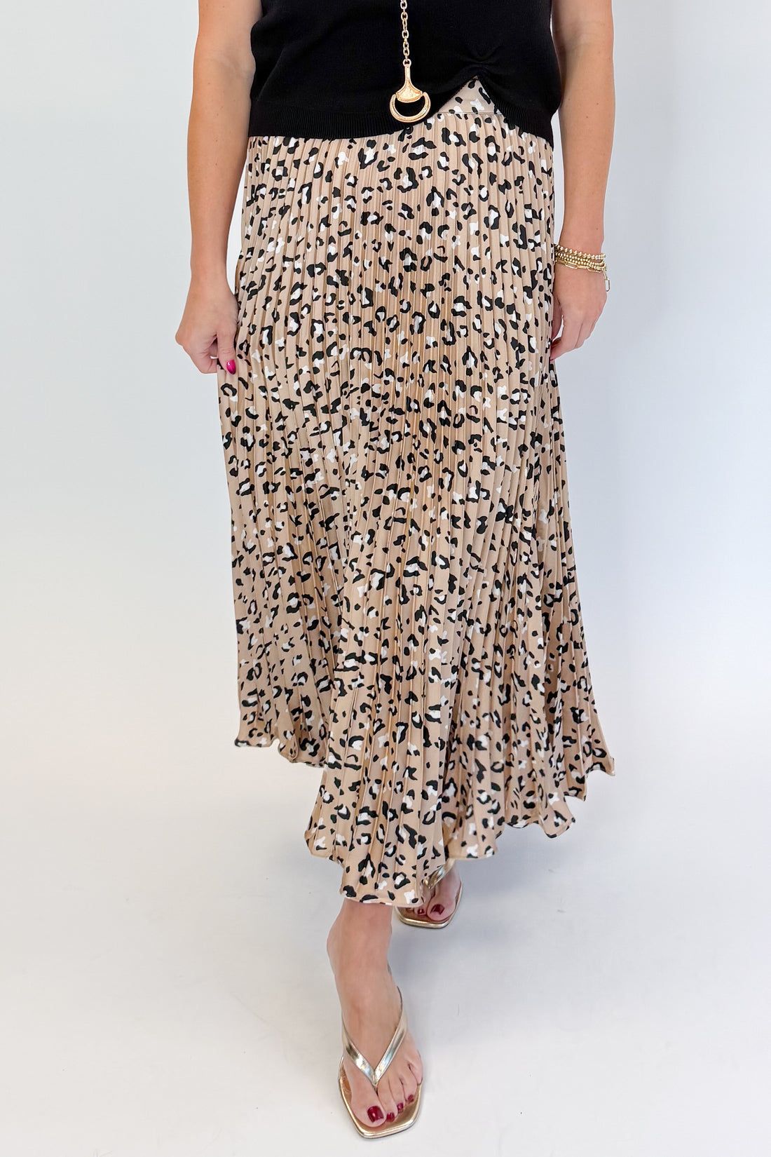 Front view of woman wearing Swagger Boutique’s Leopard Pleated Skirt &amp; Black Short Sleeve Twist Detail Sweater against white studio background.