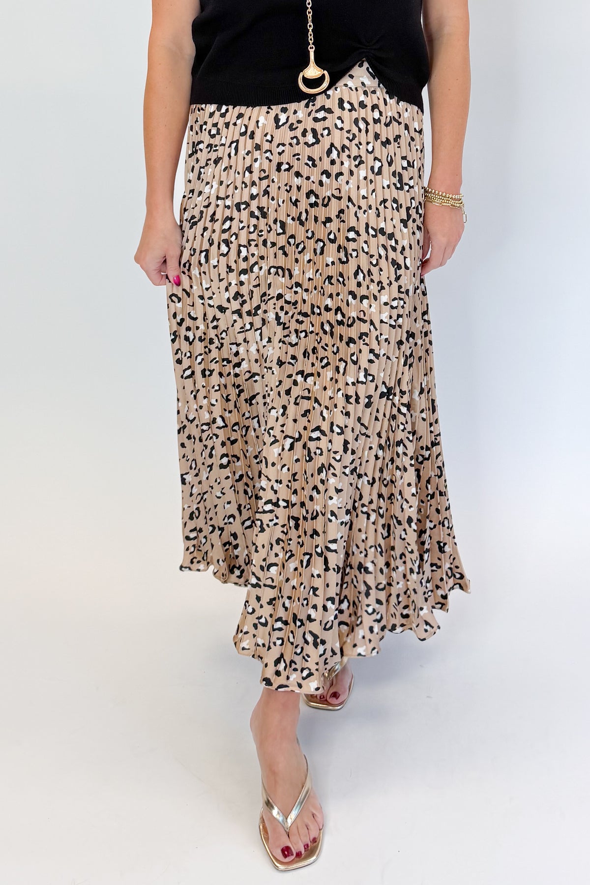 Front view of woman wearing Swagger Boutique’s Leopard Pleated Skirt &amp; Black Short Sleeve Twist Detail Sweater against white studio background.