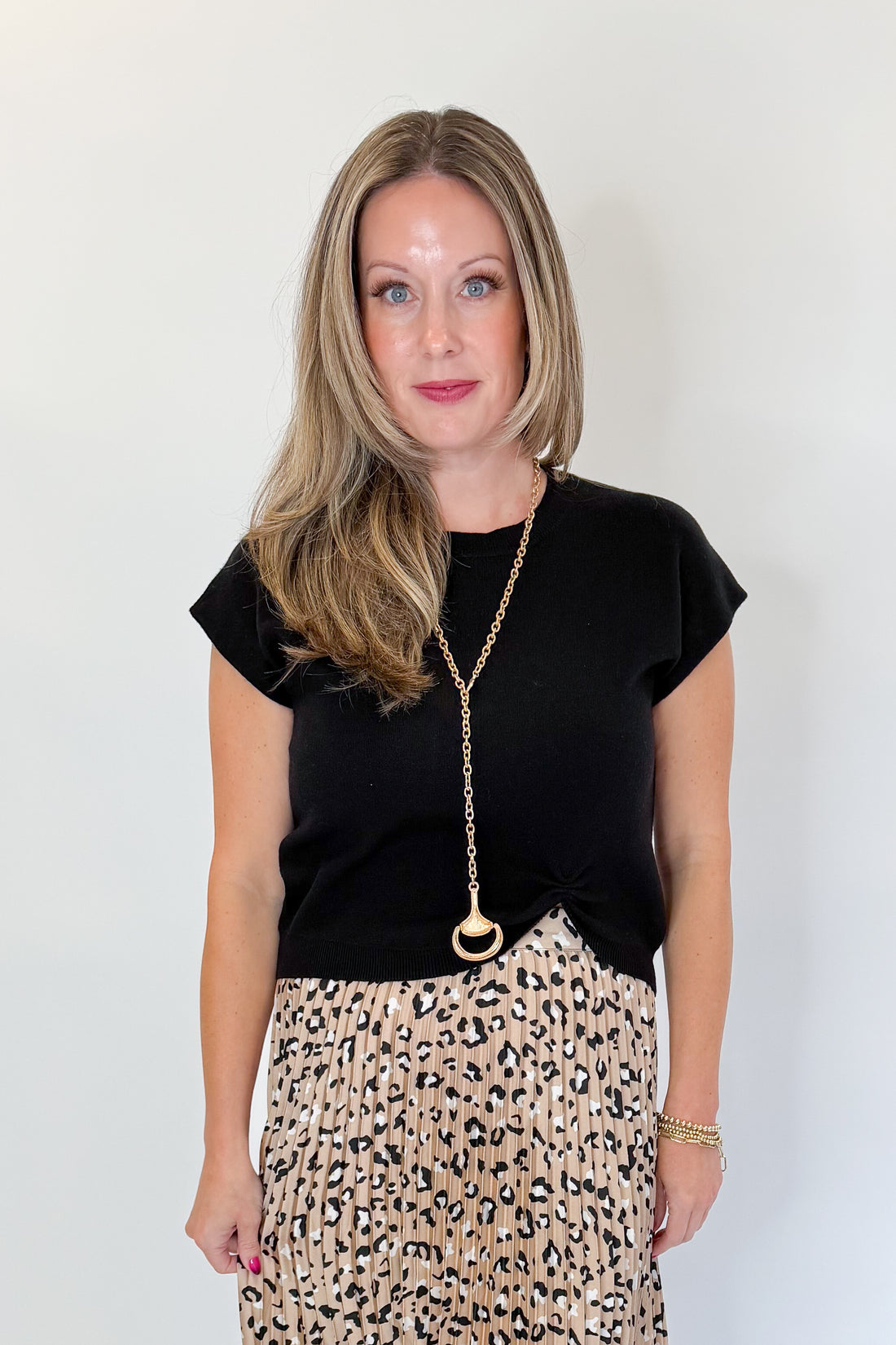 Front view of woman wearing Swagger Boutique’s Leopard Pleated Skirt &amp; Black Short Sleeve Twist Detail Sweater against white studio background.