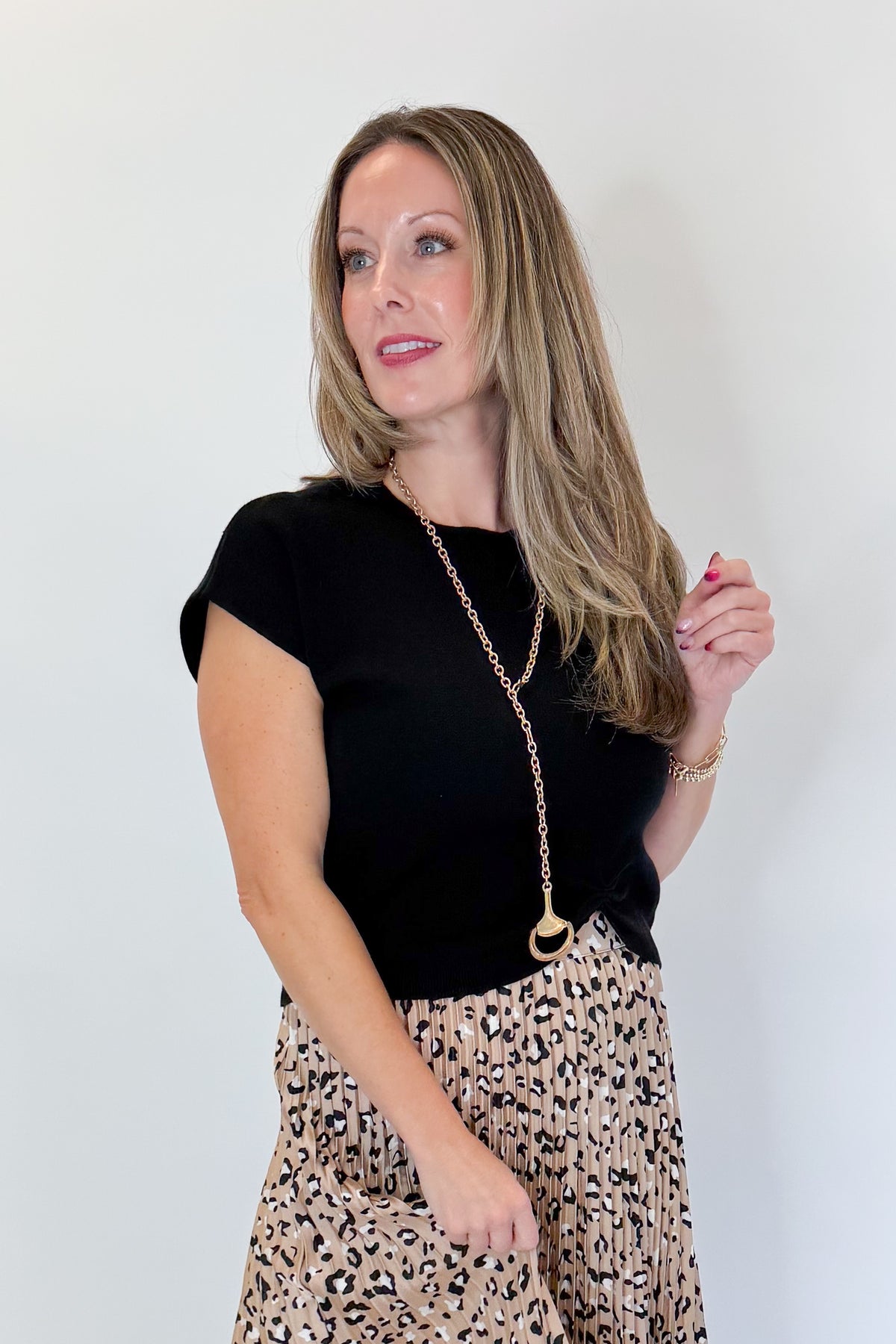 Front view of woman wearing Swagger Boutique’s Leopard Pleated Skirt &amp; Black Short Sleeve Twist Detail Sweater against white studio background.