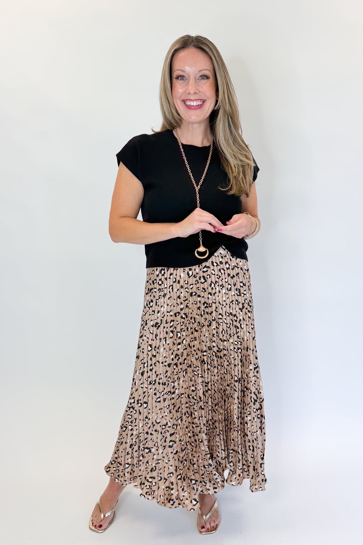 Front view of woman wearing Swagger Boutique’s Leopard Pleated Skirt &amp; Black Short Sleeve Twist Detail Sweater against white studio background.