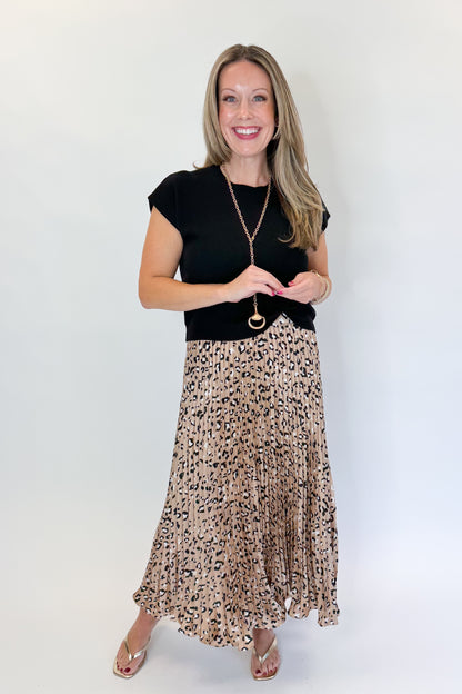 Front view of woman wearing Swagger Boutique’s Leopard Pleated Skirt &amp; Black Short Sleeve Twist Detail Sweater against white studio background.