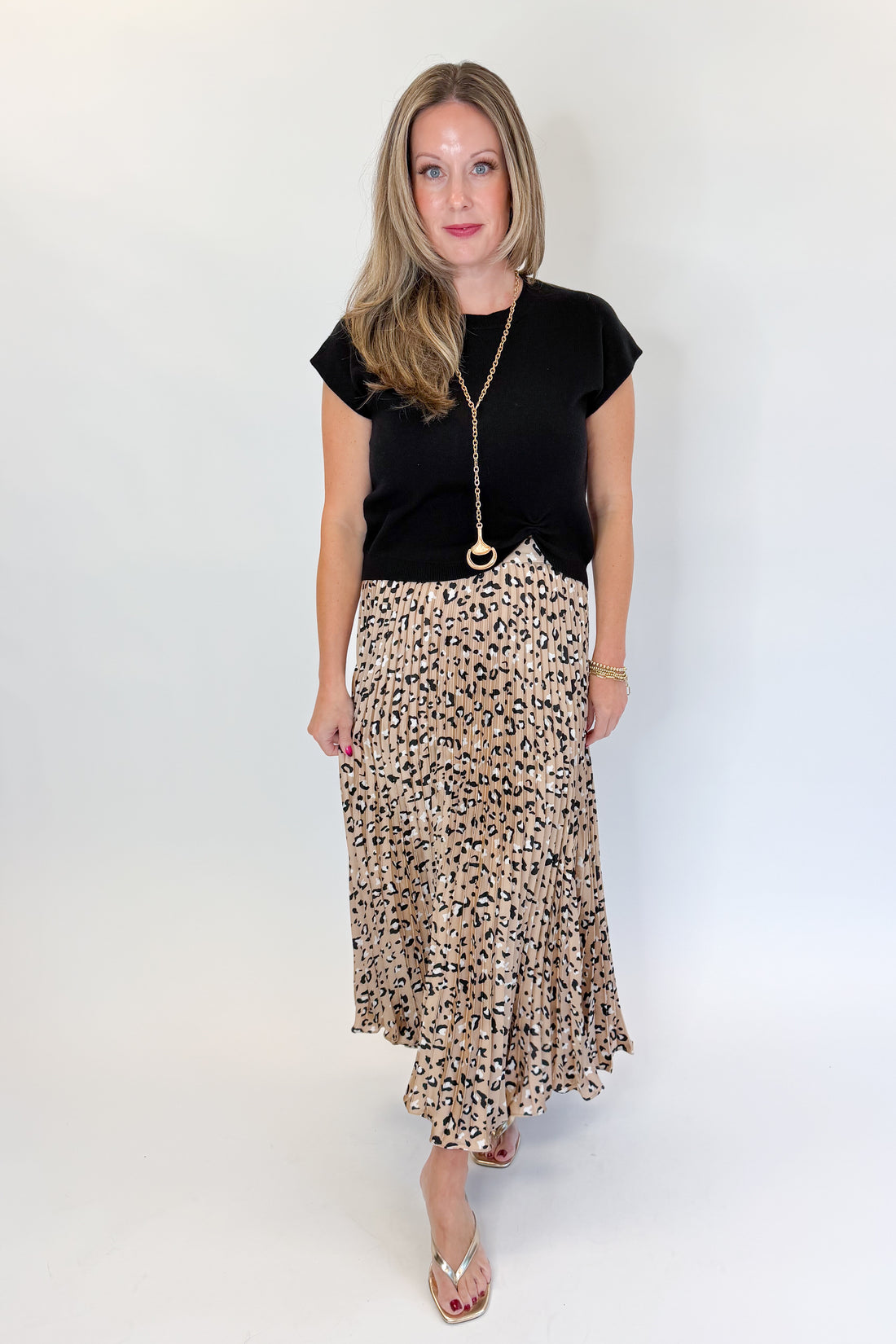 Front view of woman wearing Swagger Boutique’s Leopard Pleated Skirt &amp; Black Short Sleeve Twist Detail Sweater against white studio background.