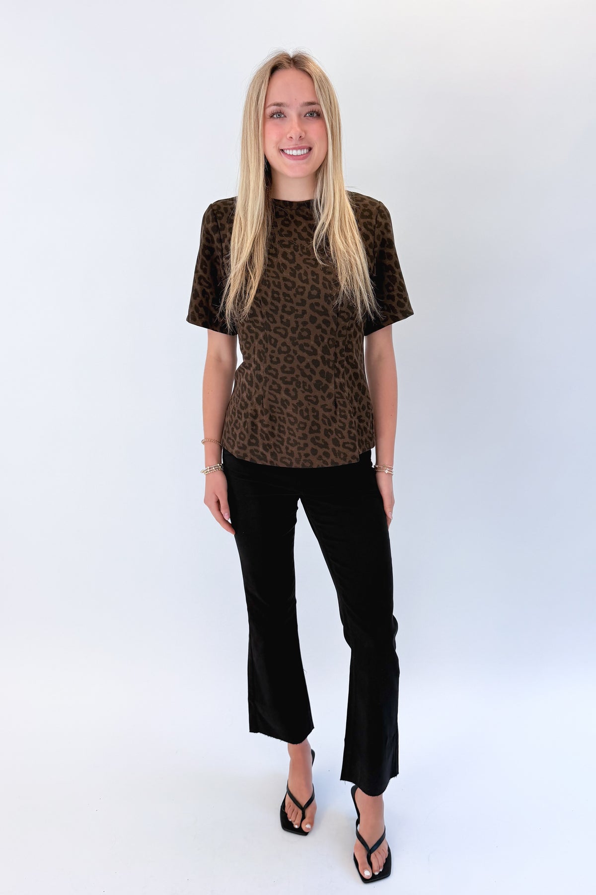Front view of woman wearing Swagger Boutique’s Leopard Pleated Top with jeans against white studio background.