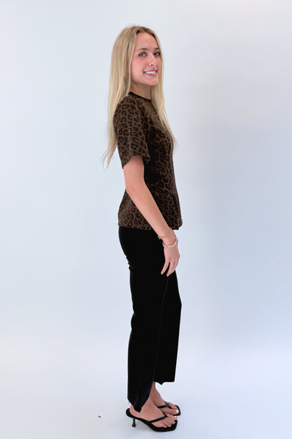 Side view of woman wearing Swagger Boutique’s Leopard Pleated Top with jeans against white studio background.