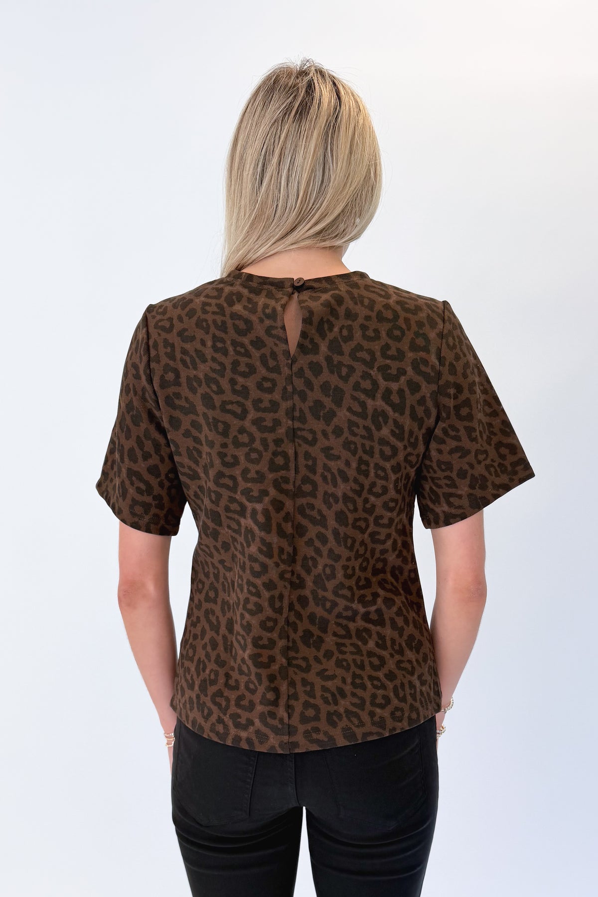 Back view of woman wearing Swagger Boutique’s Leopard Pleated Top with jeans against white studio background.
