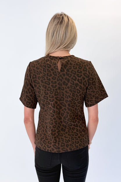 Back view of woman wearing Swagger Boutique’s Leopard Pleated Top with jeans against white studio background.